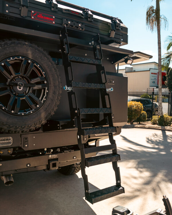 Close-up of rear of custom canopy with drop-down ladder, spare wheel carrier, lockable storage box, and The Bush Company rooftop tent by Concept Canopies