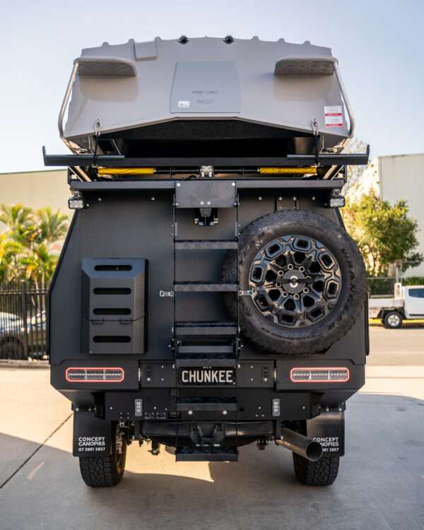 Rear view of custom canopy with drop-down ladder, lockable jerry can holders, spare wheel carrier, and boat loader with tinny on top by Concept Canopies